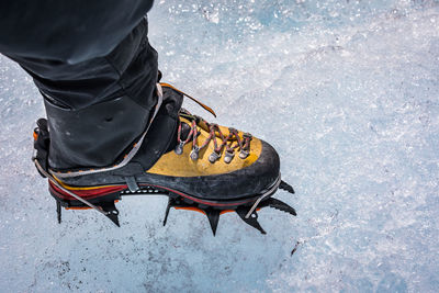 Low section of hiker wearing crampon while standing on snow