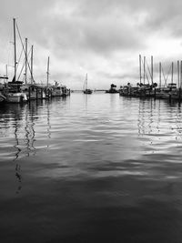 Sailboats moored at harbor against stormy sky