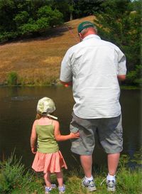 Rear view of girl standing with father fishing in lake during sunny day