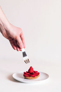 Cropped hand of person holding fork over tart over white background