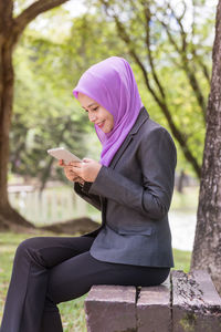 Young woman wearing hijab using mobile phone while sitting in park