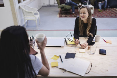 High angle view of two happy women talking to colleague at desk in office