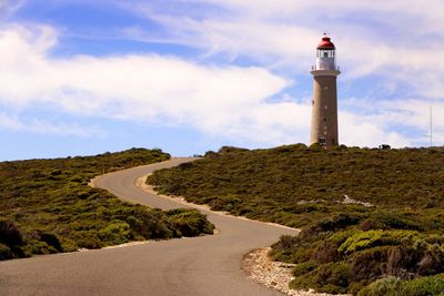 Lighthouse by road amidst buildings against sky