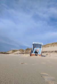 Mid adult woman sitting on hooded beach chair against blue sky