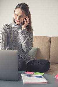 Young woman using mobile phone while sitting on sofa at home
