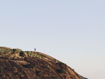 Distant view of person standing on mountain against clear sky