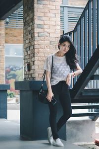 Full length portrait of woman standing against brick wall