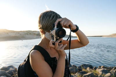 Midsection of woman photographing sea against sky