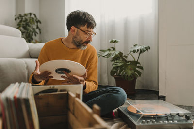 Man holding vinyl looking at record player in living room