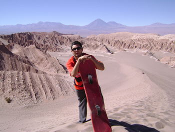 Portrait of man with sandboard standing on desert