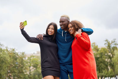 Low angle view of friends taking selfie standing outdoors