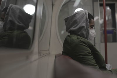 Side view of man wearing mask while sitting in train