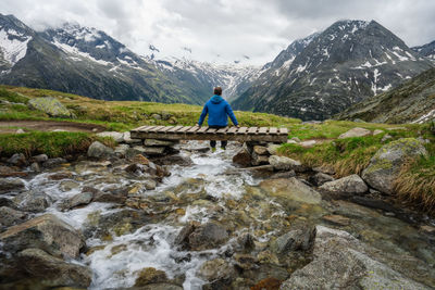 Man standing on rock by stream against sky