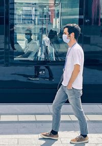 Side view of young man standing against glass wall