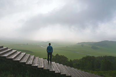 Rear view of man standing on staircase against landscape and sky