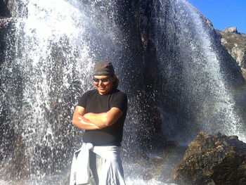 Happy man standing with arms crossed against waterfall