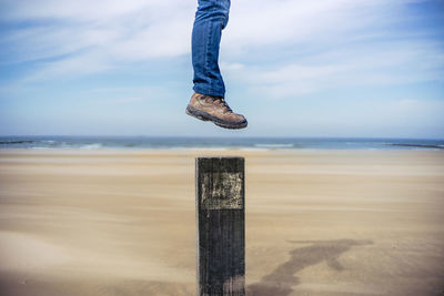 Low section of man on wooden post at beach against sky