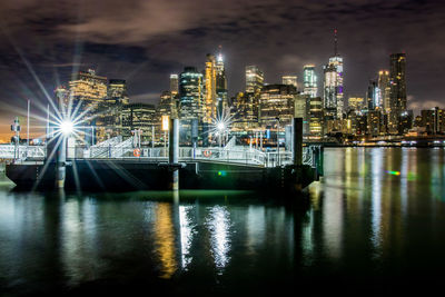 Illuminated buildings by river against sky at night