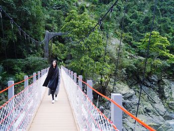 Woman walking on footbridge in forest