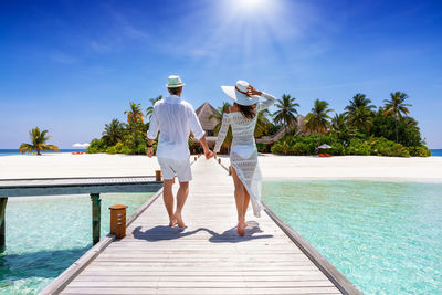 Rear view of couple walking on pier over sea against sky