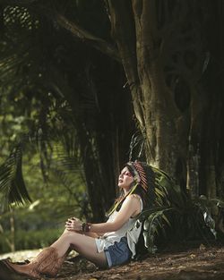 Full length of fashionable woman sitting by tree