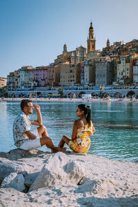 People sitting by buildings against clear sky