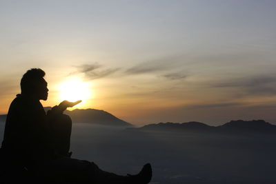 Silhouette man sitting against sky during sunset