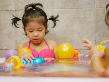 Cute girls with toys sitting in bathtub