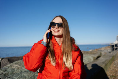 Young woman wearing sunglasses standing at beach against clear sky
