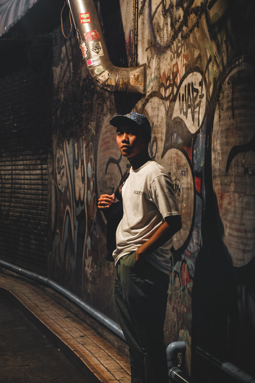 one person, real people, graffiti, young adult, young men, standing, lifestyles, architecture, casual clothing, wall - building feature, art and craft, clothing, creativity, leisure activity, three quarter length, looking, built structure, men, indoors, brick