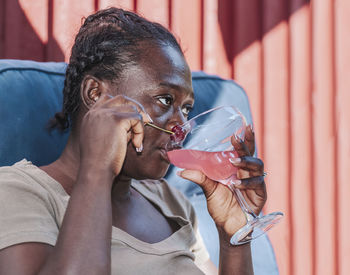 African woman sitting with a cherry drink outdoors and cooling off in the shade on a hot sunny day.