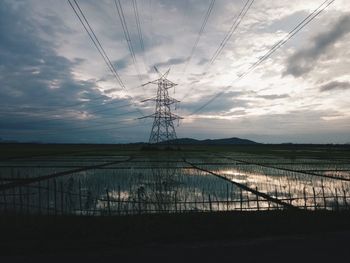 Electricity pylon by lake against sky