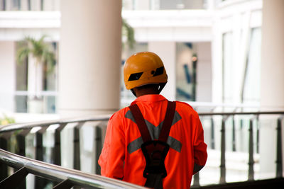 Rear view of manual worker wearing workwear standing by railing