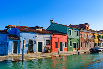 Houses by canal against clear blue sky