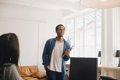 Smiling computer hacker looking away while standing in creative office