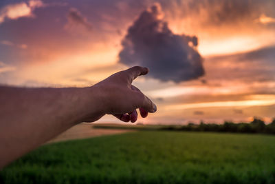 Cropped hand of man pointing towards sky during sunset