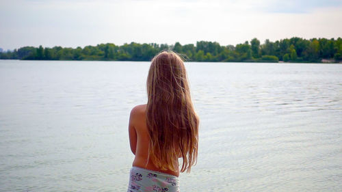 Rear view of woman standing by sea against sky