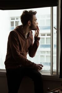 Man smoking cigarette by window sill