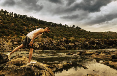 Side view of man standing on rock against sky