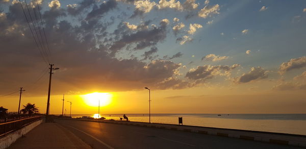 Road by sea against sky during sunset