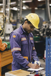 Male blue-collar worker writing in notepad while working in industry