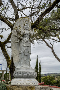 Low angle view of goddess statue against tree and sky