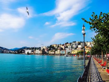 View of city at waterfront against cloudy sky