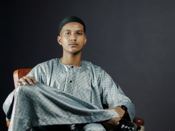 Portrait of young man sitting against black background