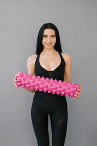 Fitness a woman in sports black clothes with a massage roller or a roll in her hands smiles