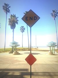 Road sign by palm trees against sky