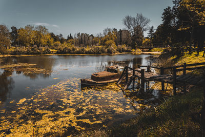 Old rusty abandoned wrecked ship tied up to a broken wooden dock in a small lake