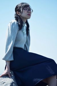 Young woman sitting on blue against sky