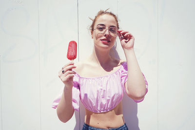 Portrait of beautiful woman having popsicle by white wall