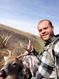 Portrait of man with deer crouching on field against sky